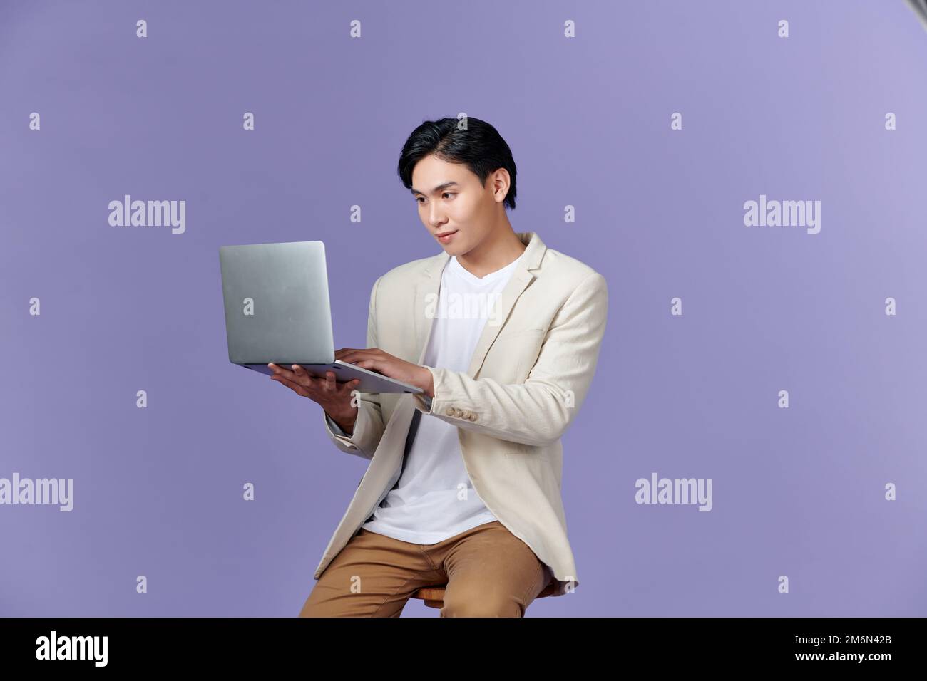 Portrait of young Asian businessman standing and holding laptop computer Stock Photo