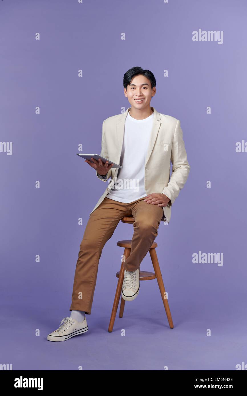 Handsome young man holding digital tablet and looking at it with smile while standing against purple background Stock Photo
