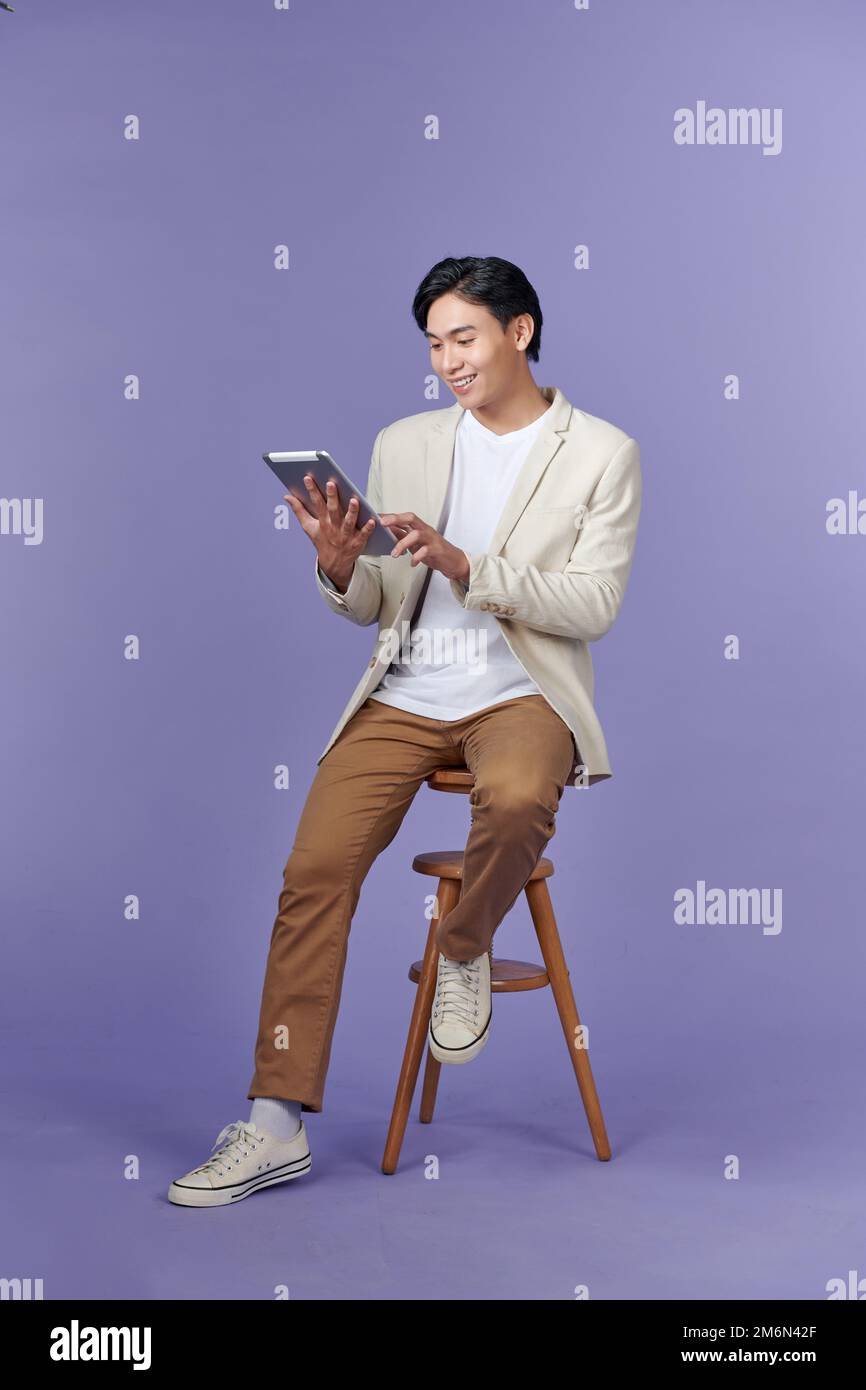 Happy attractive young man standing and using tablet over purple background Stock Photo