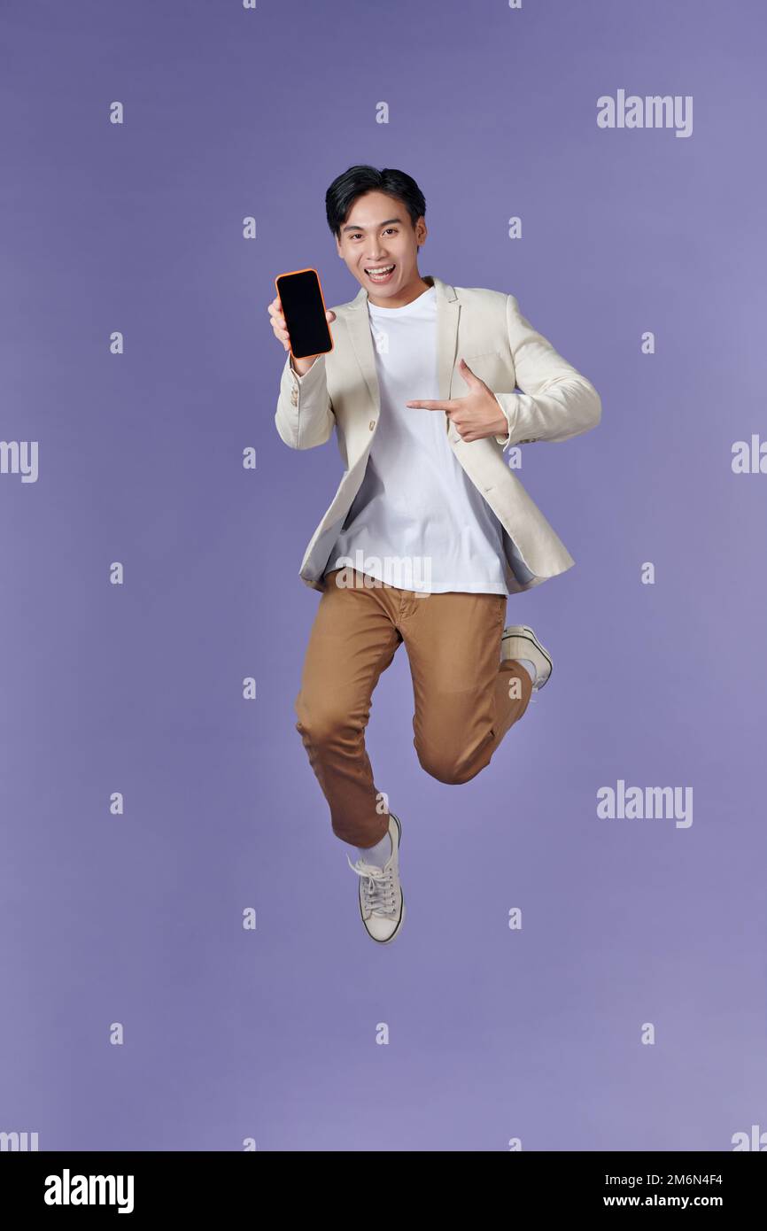 Excited young man guy jumping point index finger on mobile phone with blank empty screen Stock Photo