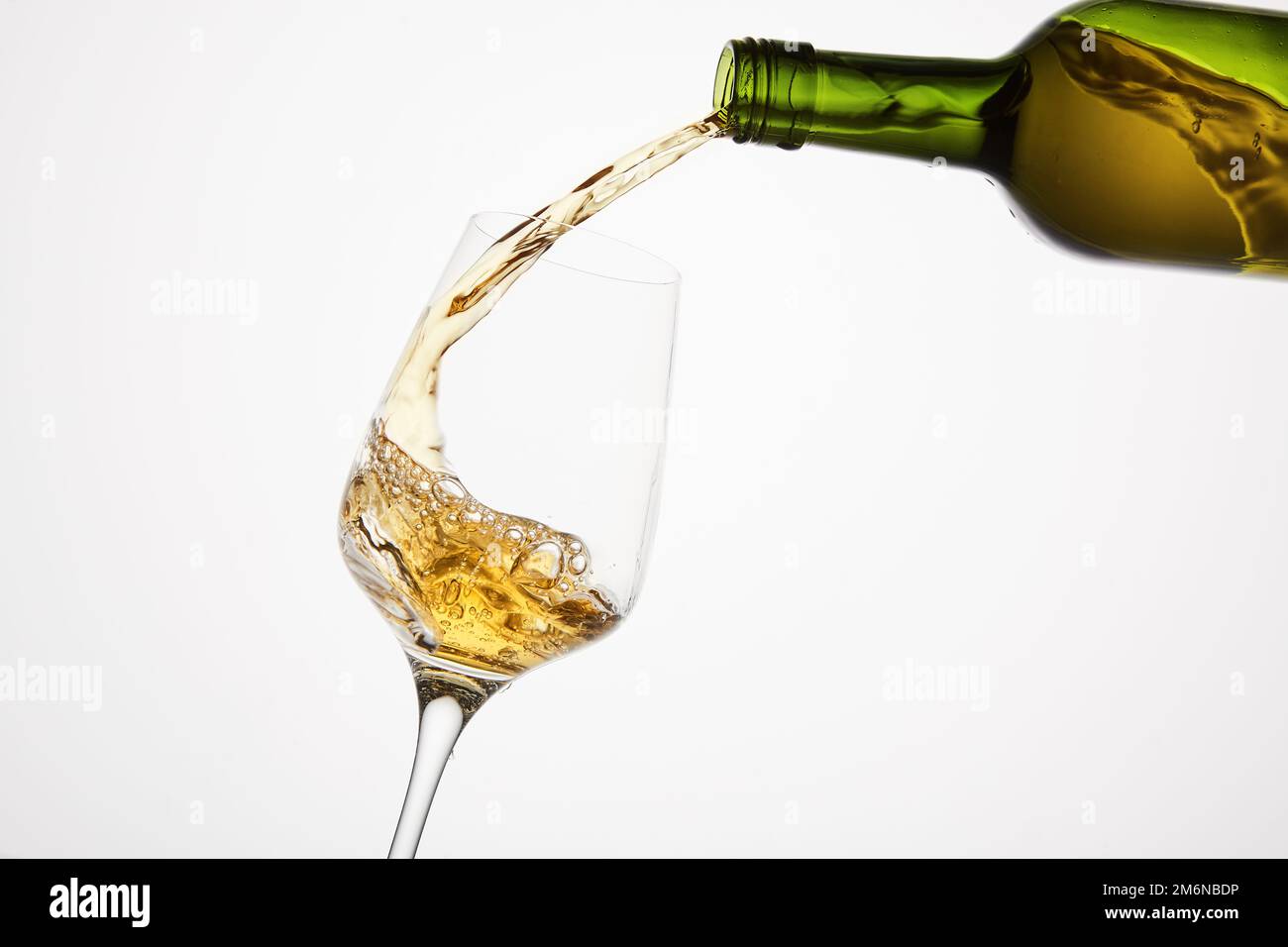 White wine pouring from neck of green bottle without label to tilted