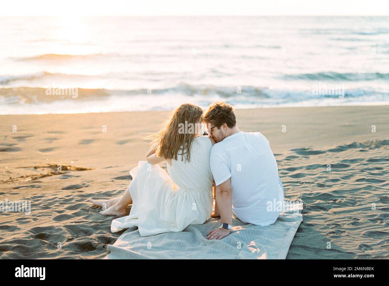 Man kissing woman shoulder while sitting on a blanket on the beach Stock Photo Alamy