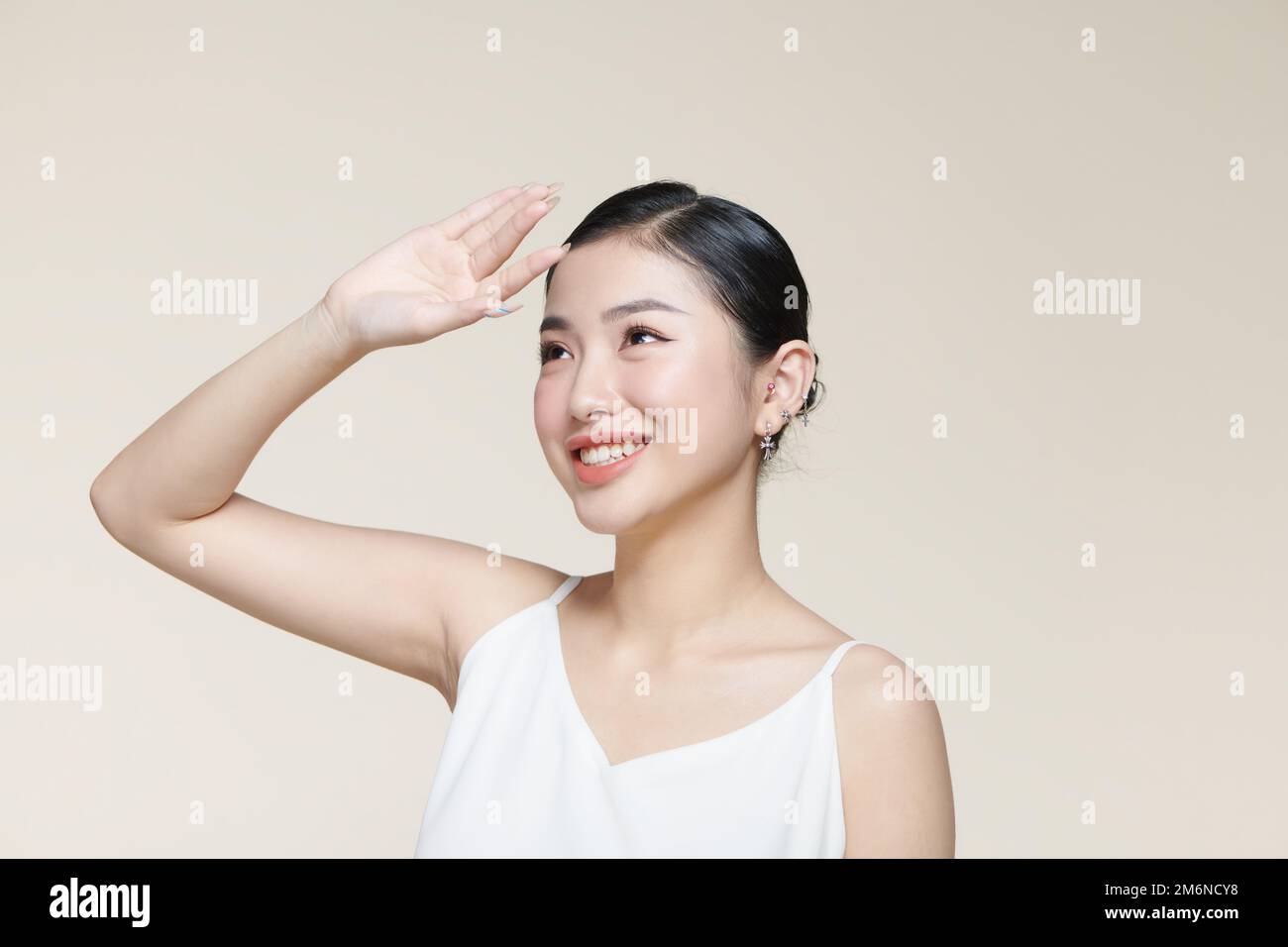 Young asian woman raising hand to covering her face from sunlight against a beige background Stock Photo