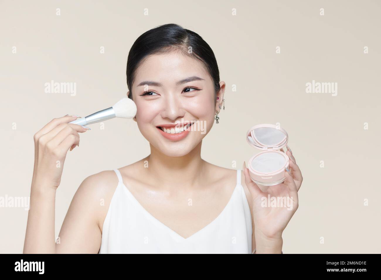 Portrait of beautiful young woman looking at the mirror putting on makeup holding a makeup brush Stock Photo