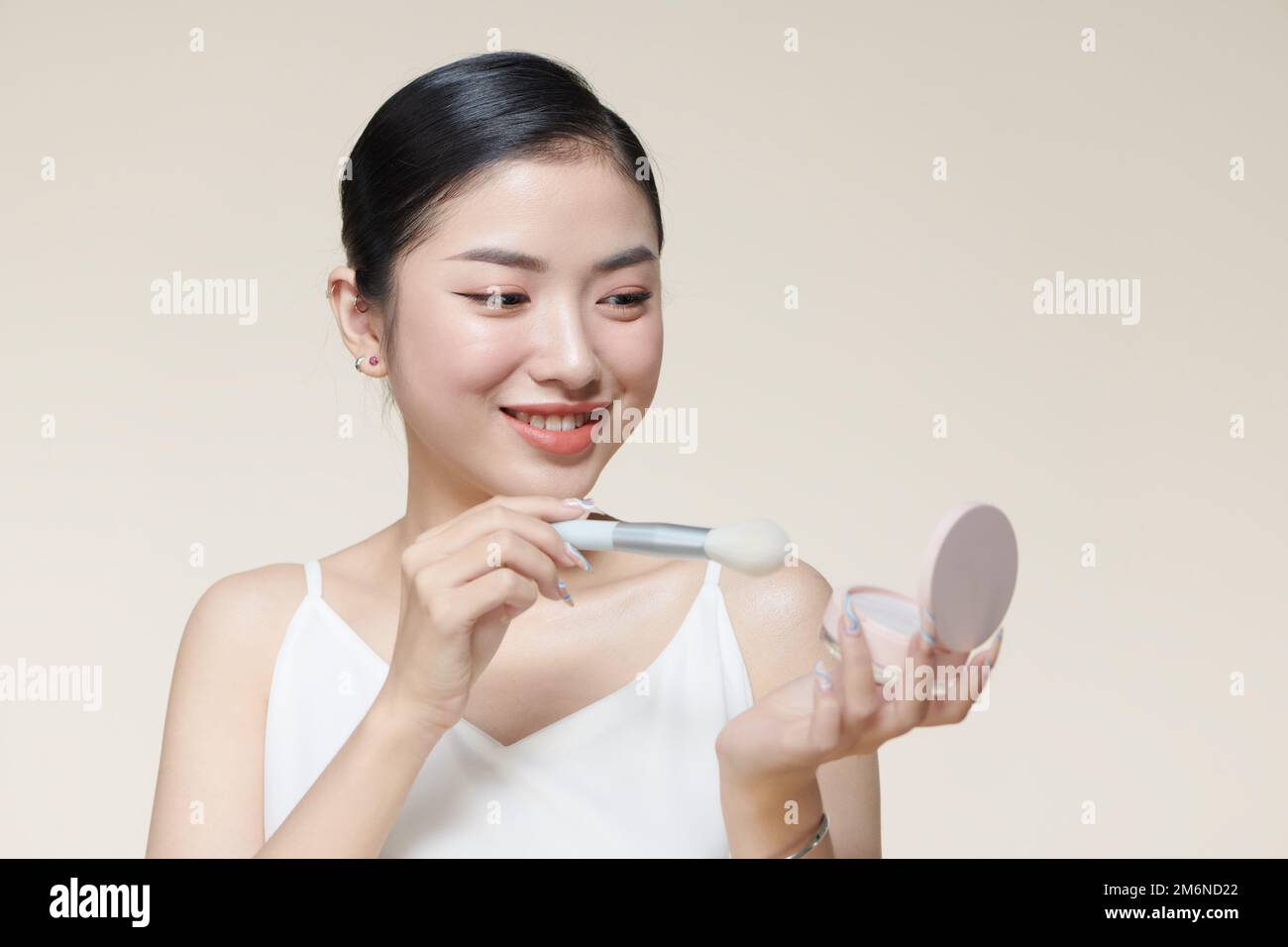 Young woman with makeup holding powder brush against baige background Stock Photo