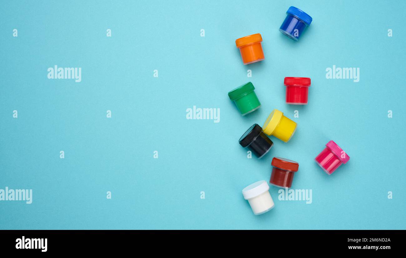 Plastic jars with multi-colored gouache on a blue background Stock Photo