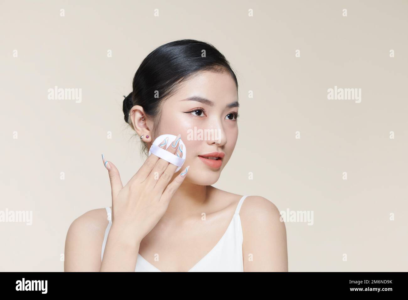 Beautiful young woman applying face powder with puff applicator over beige background Stock Photo