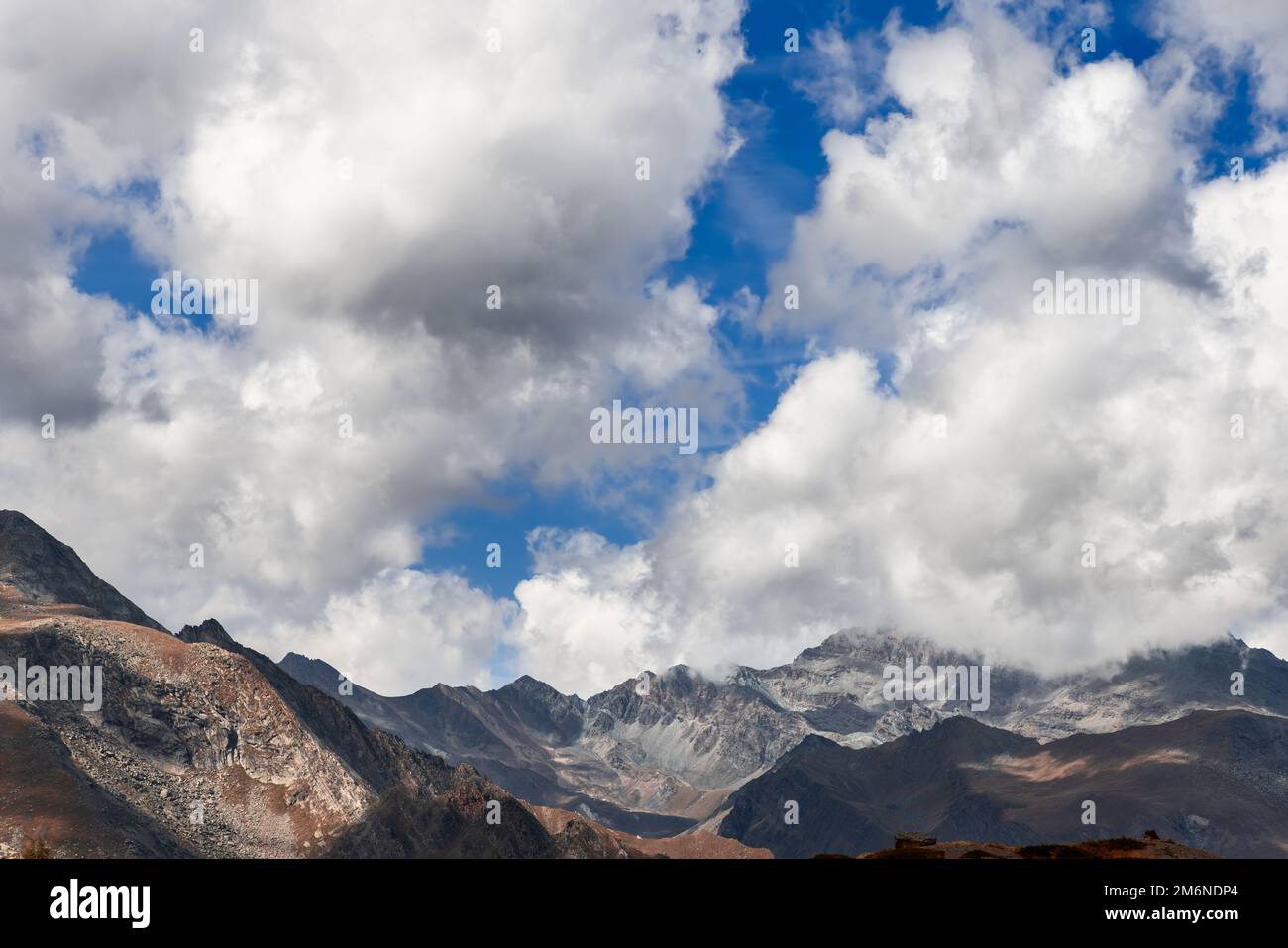 Heavy white clouds in blue sky leave shadows on granite slopes of alpine mountains in Parco Nazionale Gran Paradiso in autumn, Aosta Valley, Italy Stock Photo