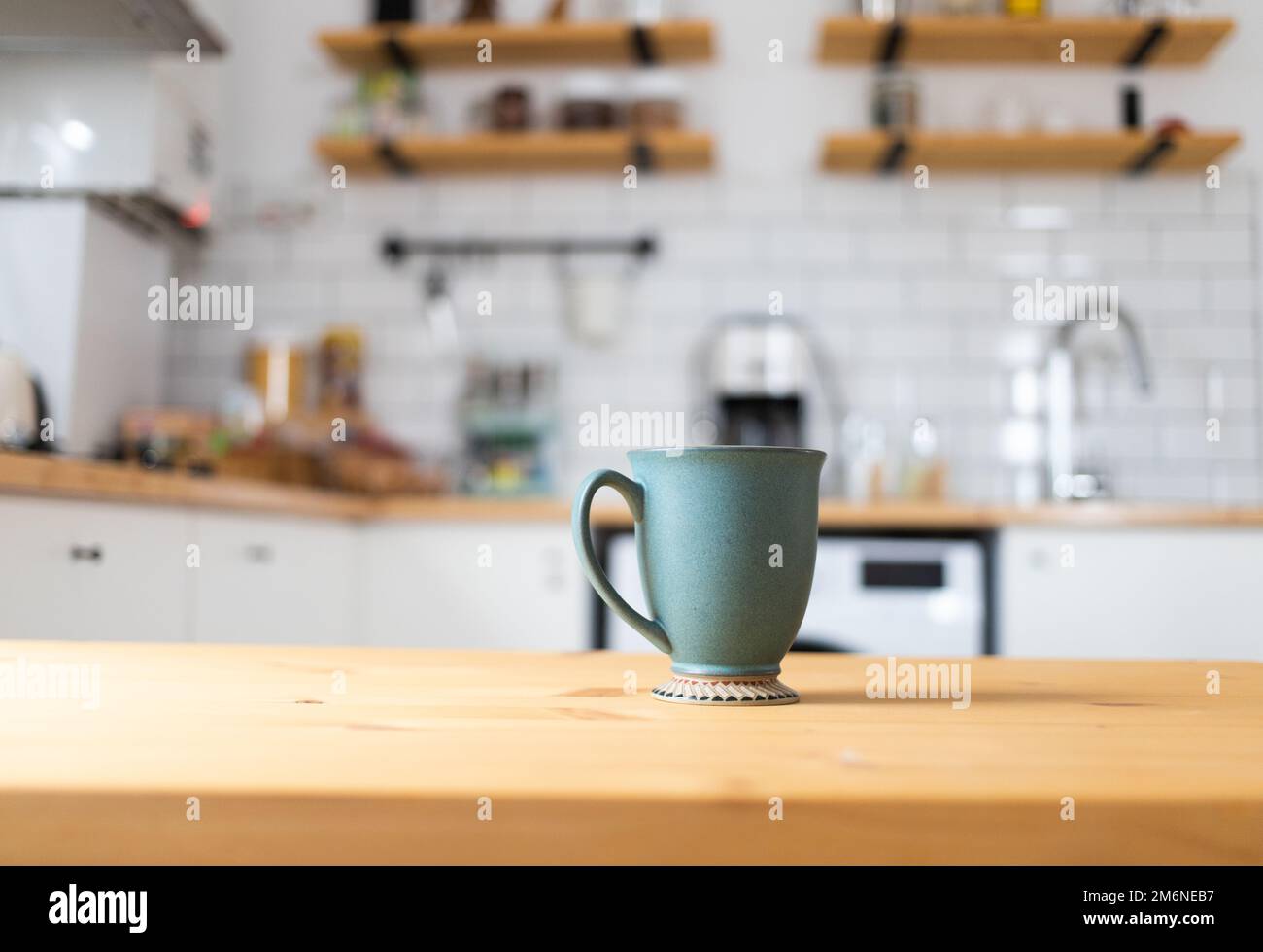 Green coffee cup on kitchen table blurred kitchen in background Stock Photo