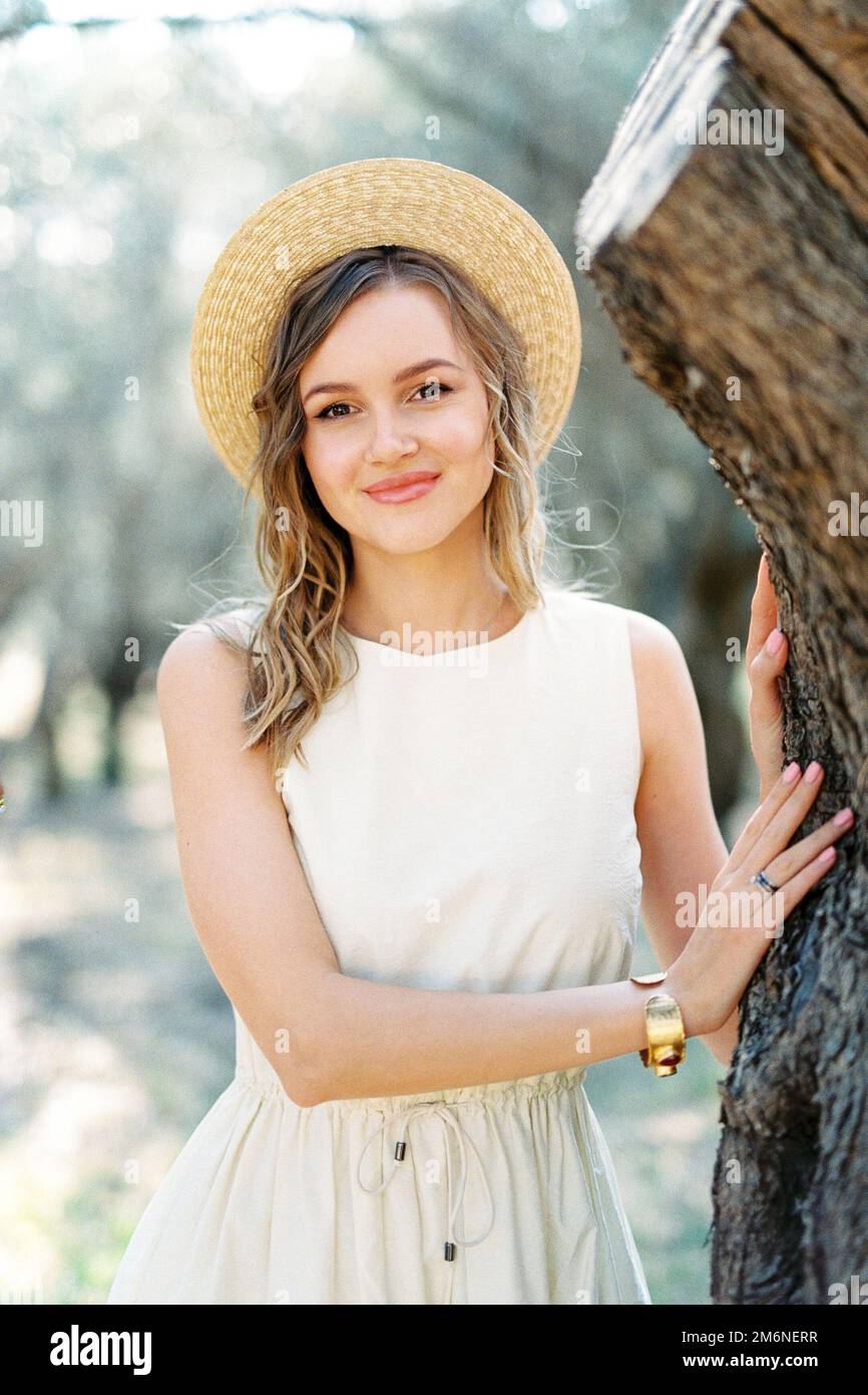 Girl in a straw hat stands near a tree in an olive grove. Portrait ...