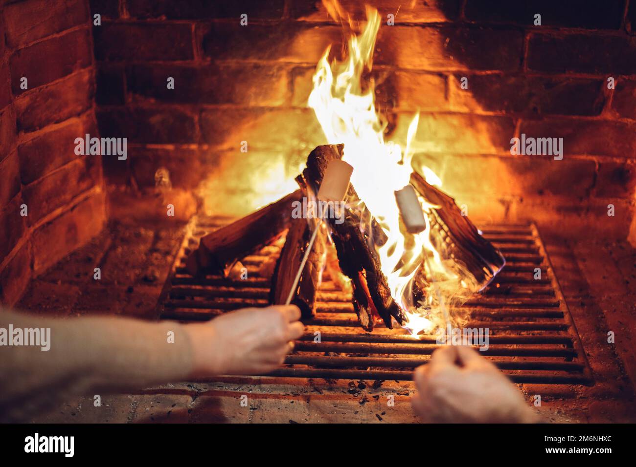 People toasting marshmallow on chopsticks over fireplace in cozy house