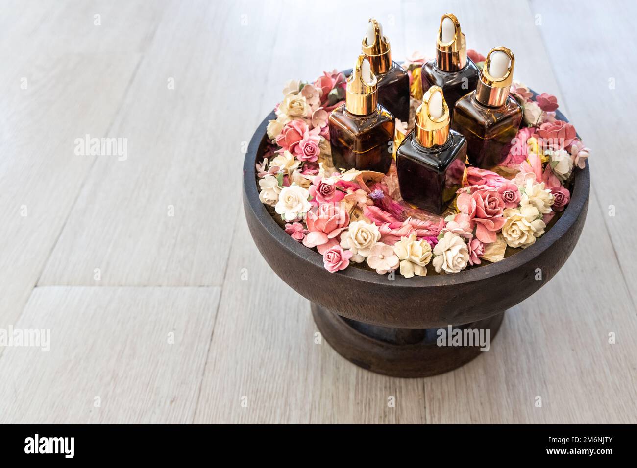 Various essential oil dispenser on tray surrounded with rose petals for massage and spa on wooden surface Stock Photo