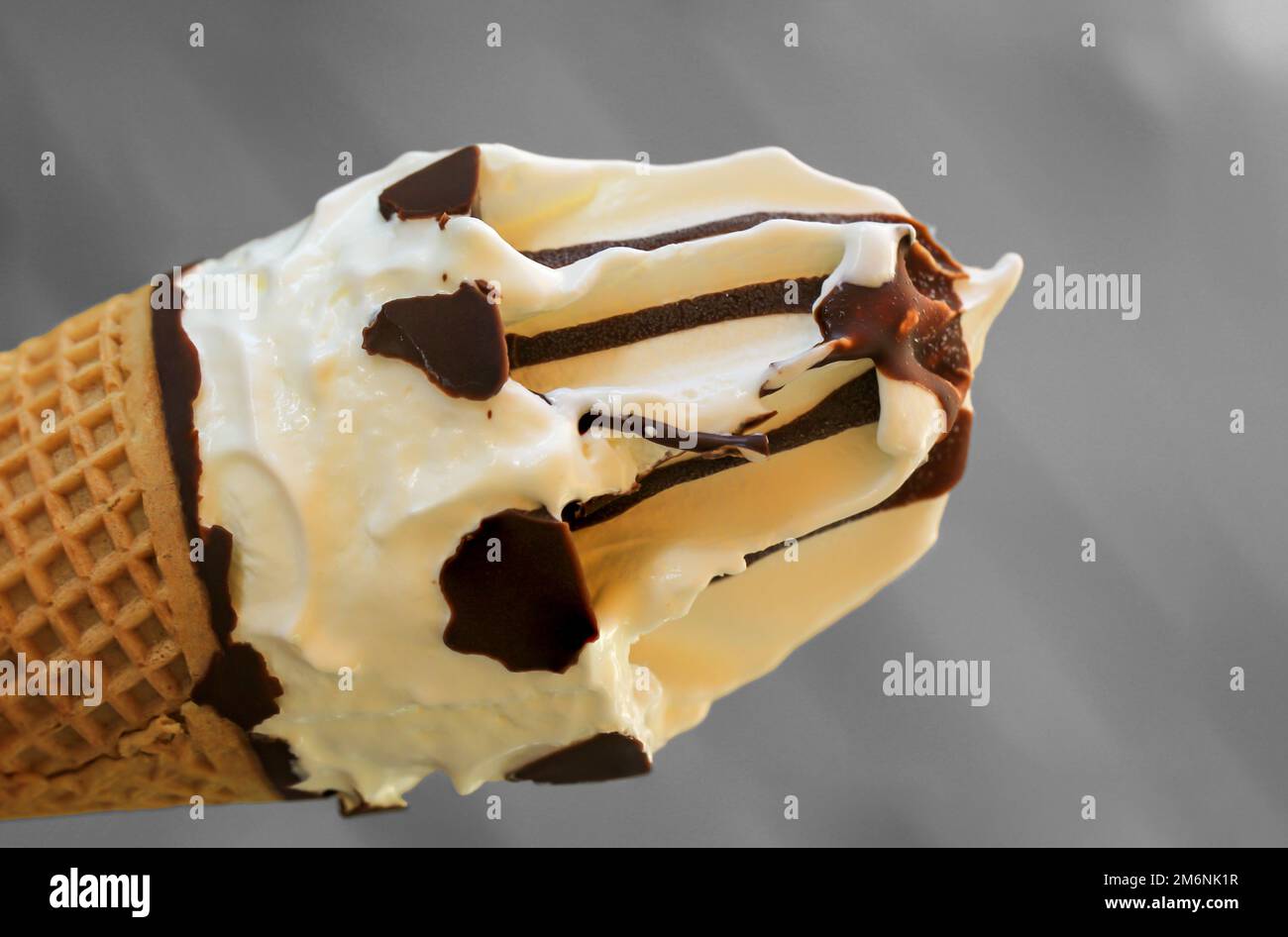 A close up of an ice cream cone with vanilla ice cream and chocolate icing. Stock Photo