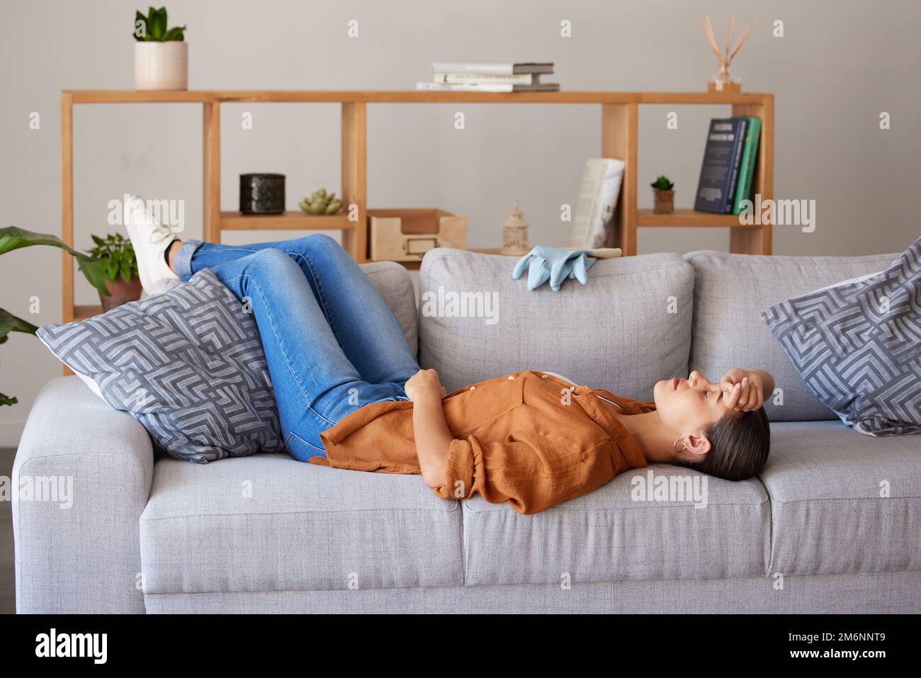 Tired cleaner woman, sleep and sofa to relax for fatigue, wellness and mental health after cleaning house. Hygiene expert, burnout and sleeping on Stock Photo