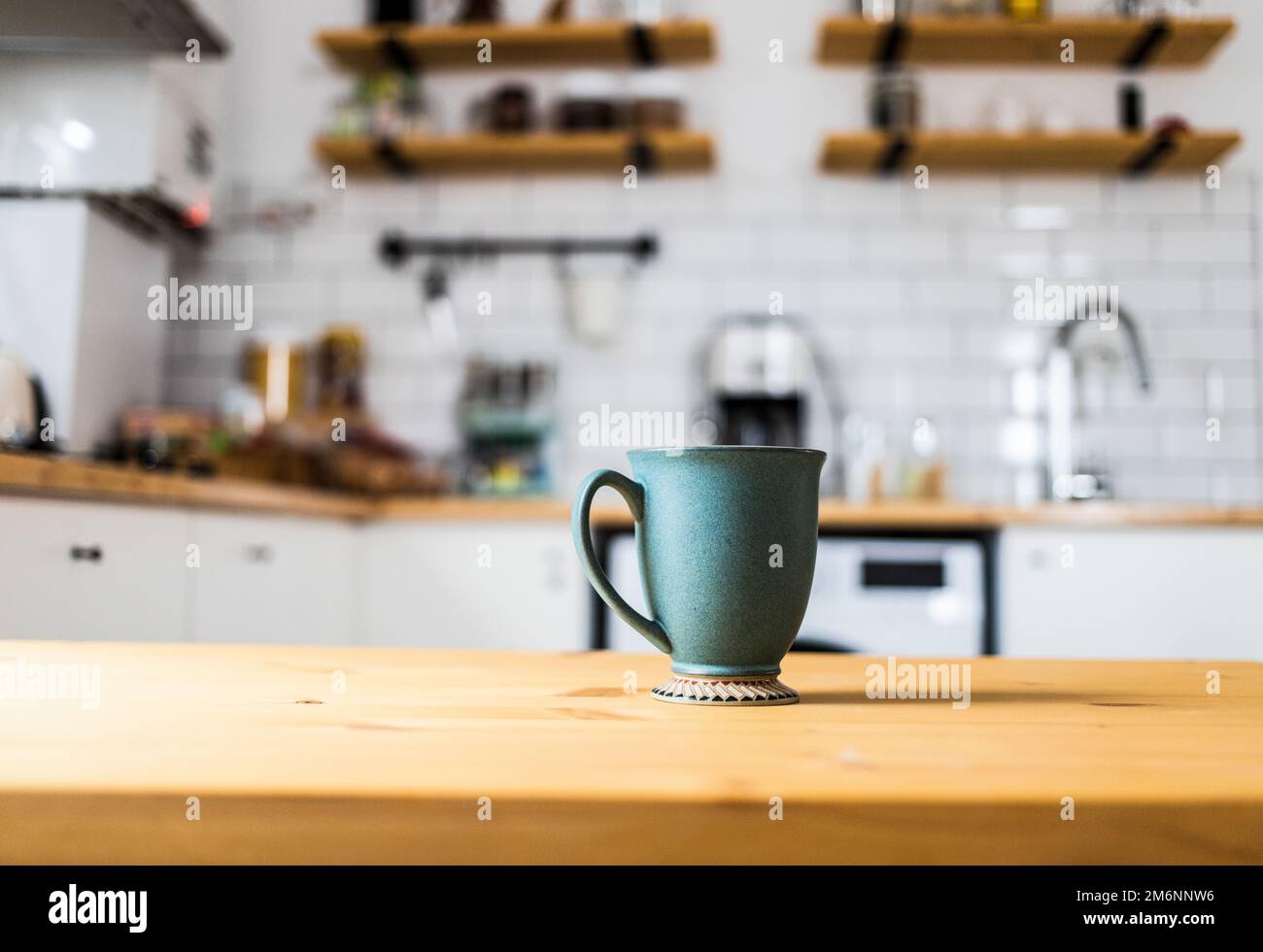 Green coffee cup on kitchen table blurred kitchen in background Stock Photo