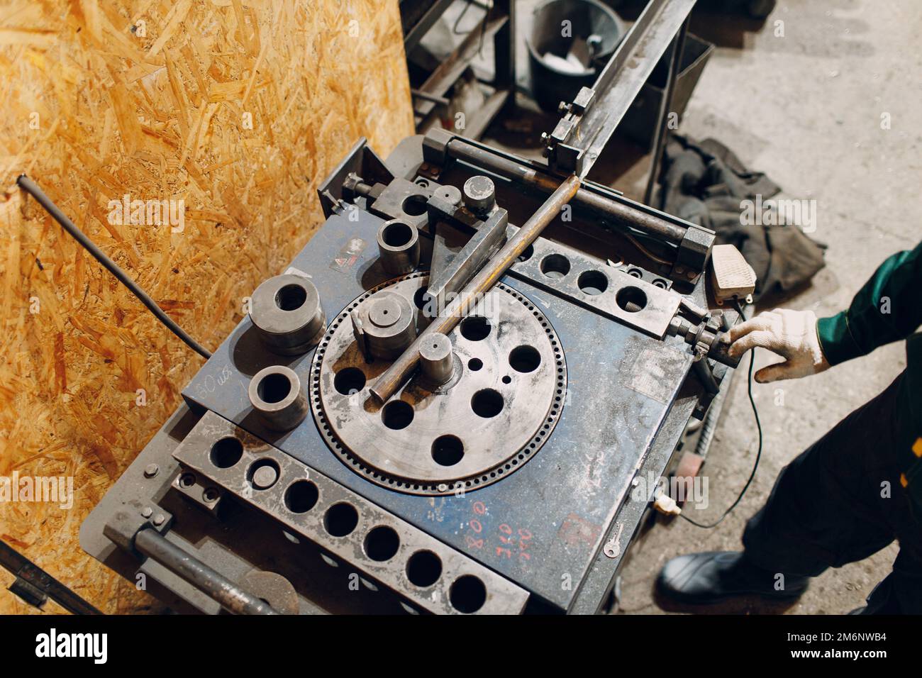 Worker at factory with industrial machine for bending of metal pipes ...