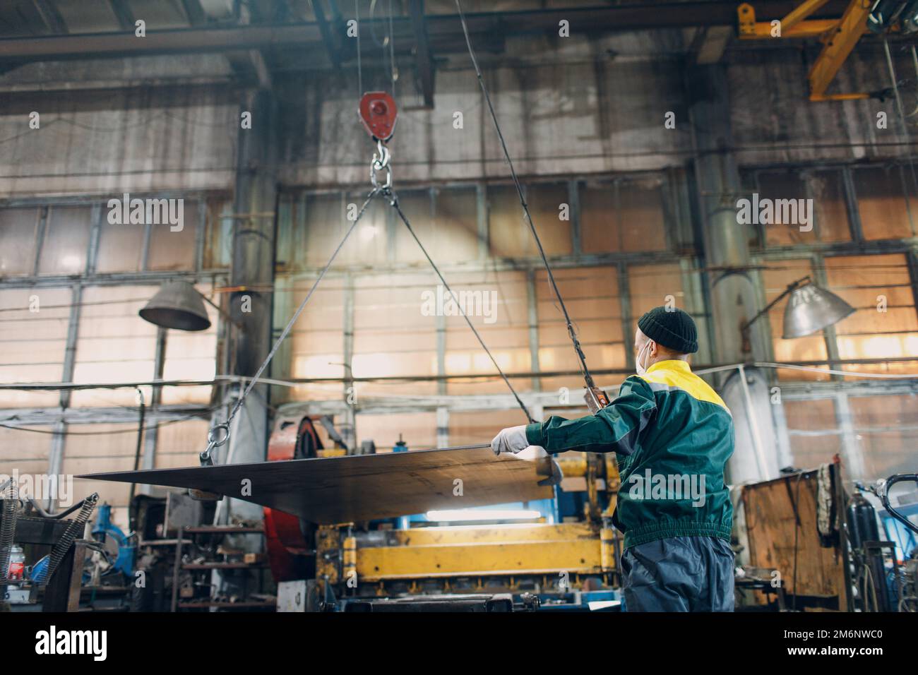 Worker lift metal sheet with crane chain hoist with remote controller and hook at industrial factory plant. Stock Photo