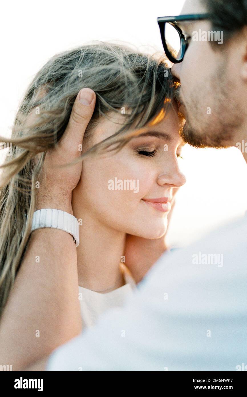 Man kisses woman on the forehead, holding her head in his hands. Portrait Stock Photo