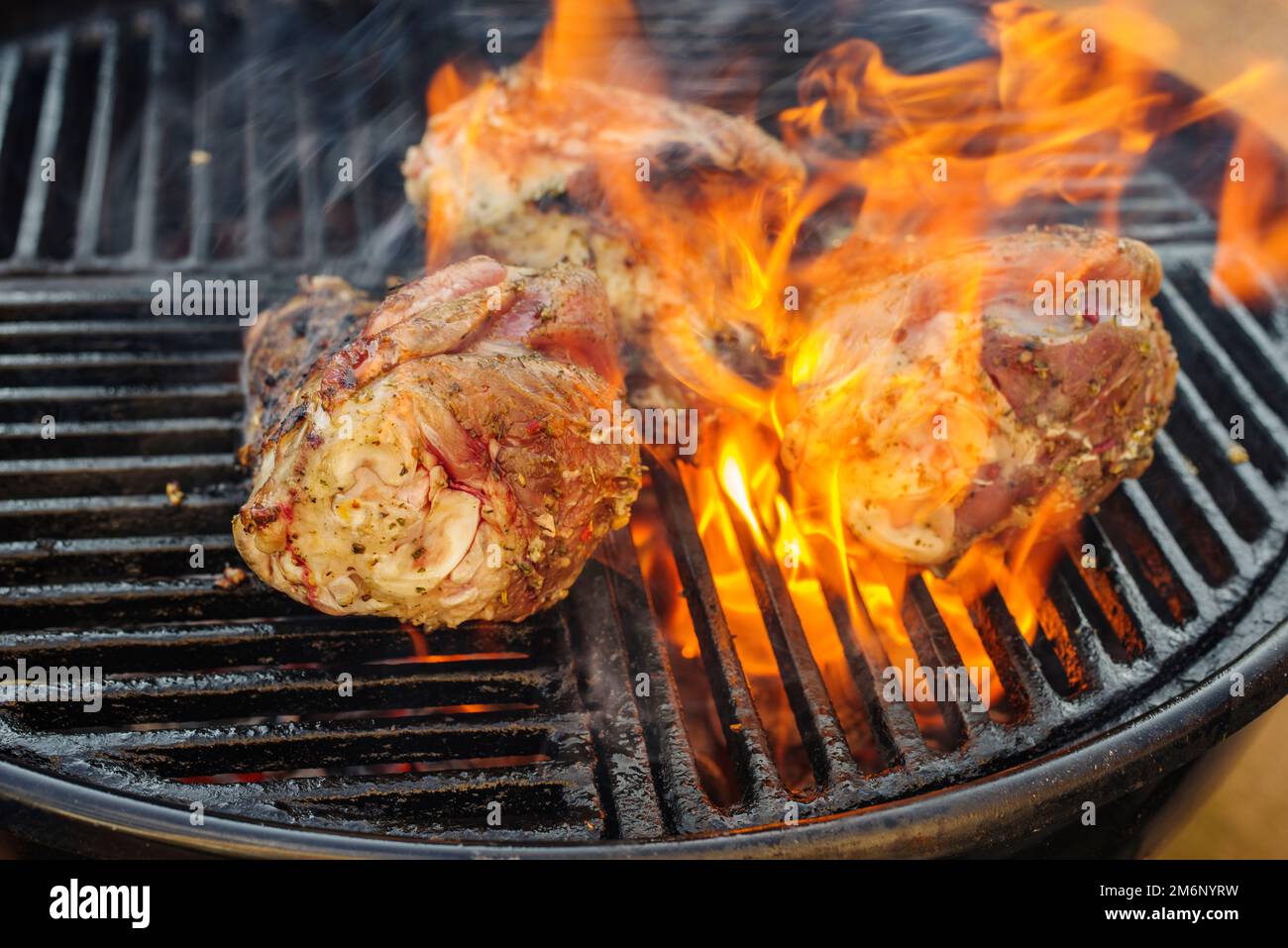 Traditional barbecue lamb shank grilled as close-up on a charcoal grill with fire and smoke Stock Photo