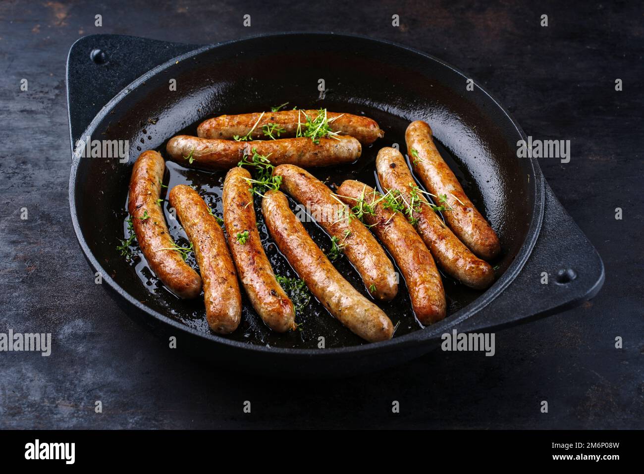 Traditional fried German pork bratwurst with cress served as close-up in cast iron design skillet on a rustic black board Stock Photo