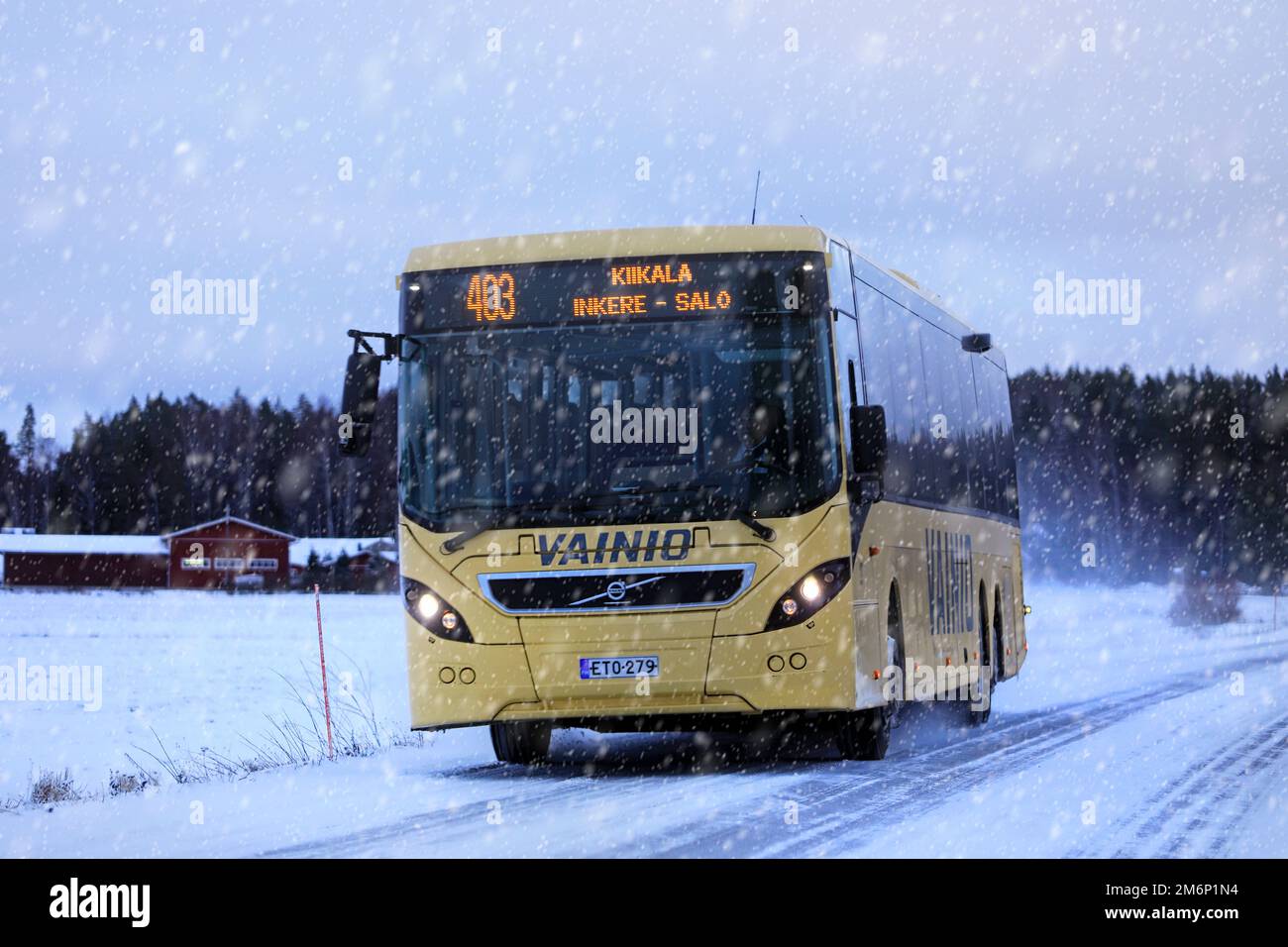 Yellow Volvo bus transports passengers along road in winter snowfall. Salo, Finland. December 28, 2022. Stock Photo