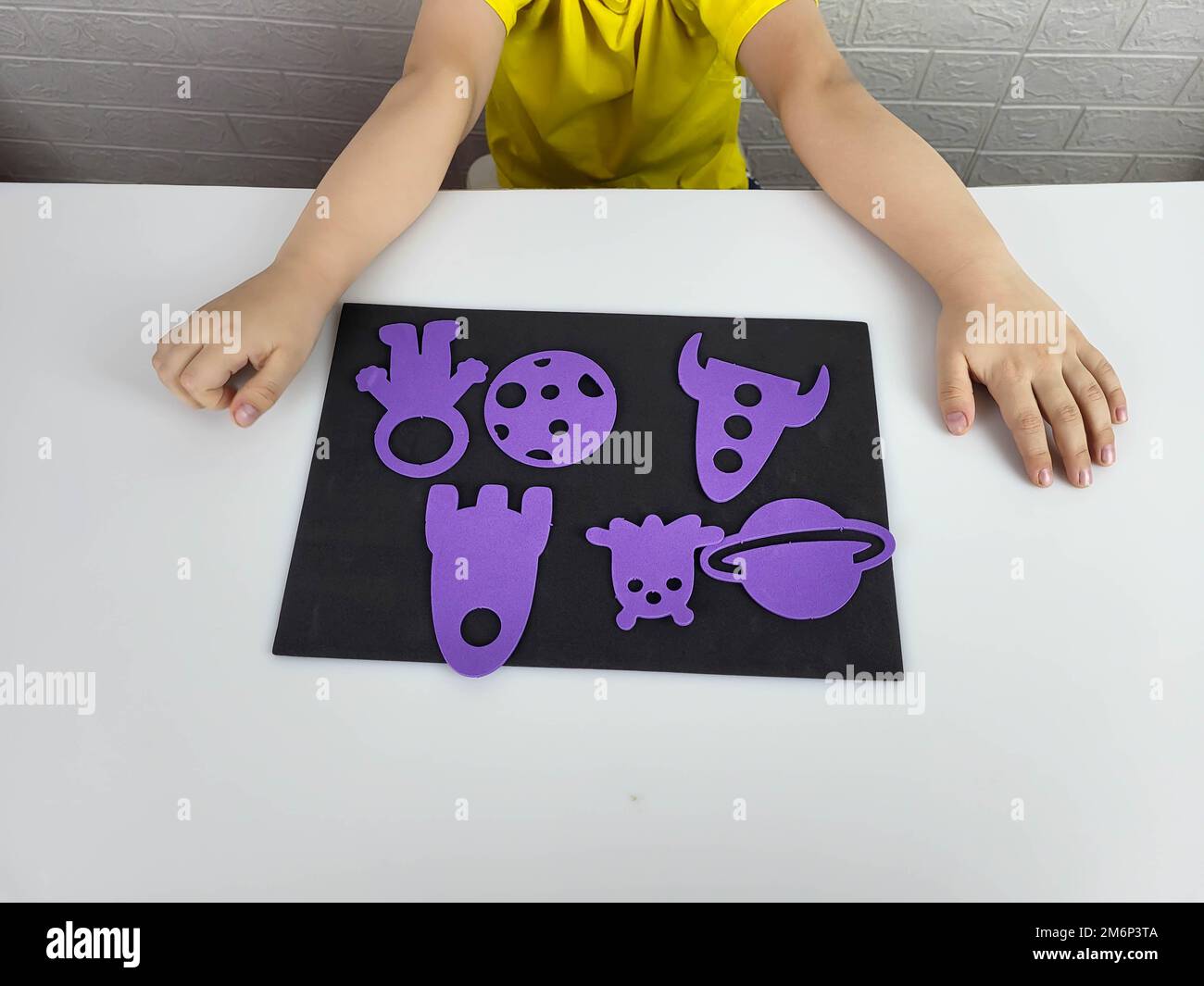Children's hands are folding the application on a black background lilac rockets, planets, cosmonaut for the Cosmonautics Day Stock Photo