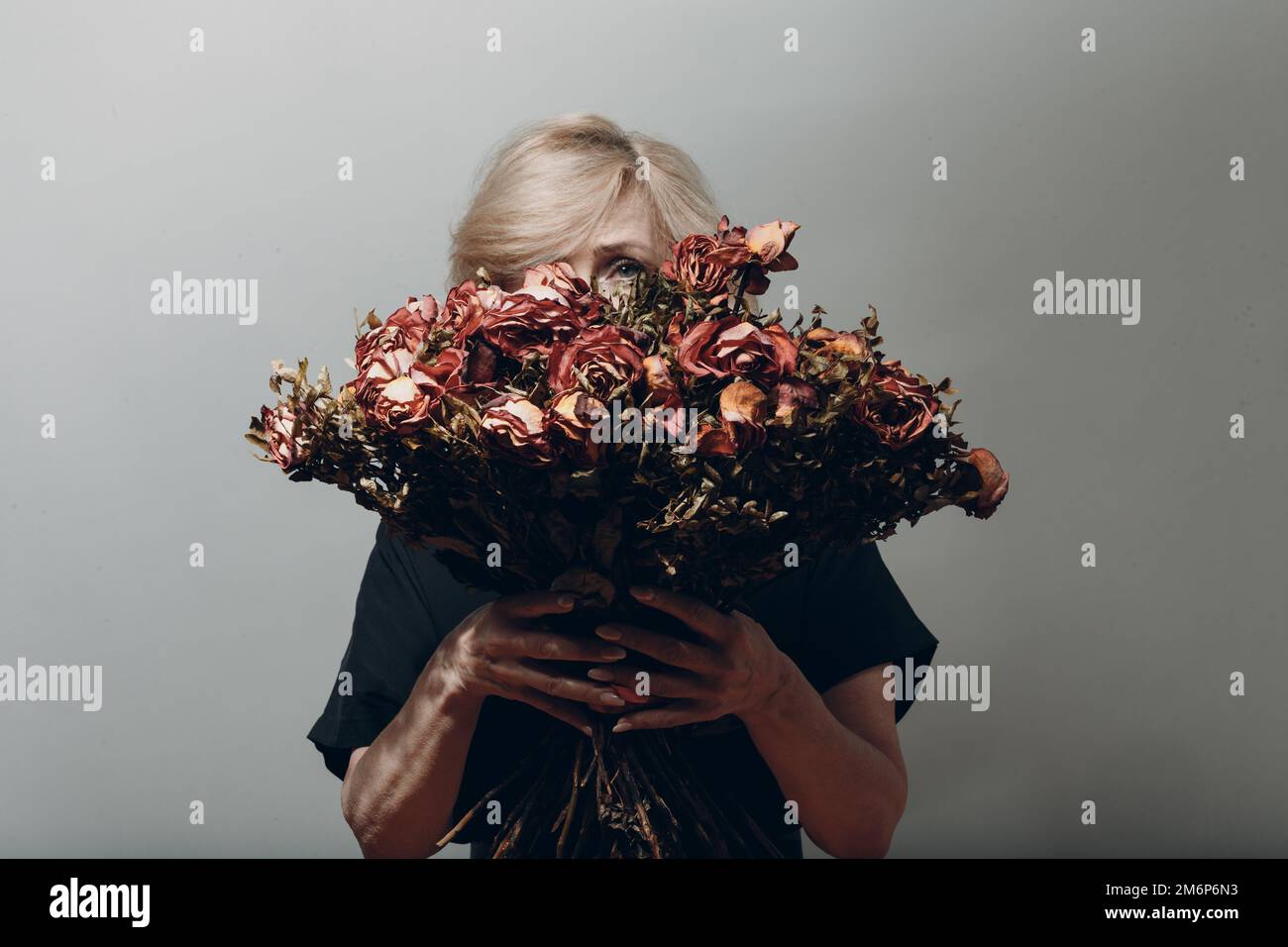 Upset elderly woman hold withered dry old rose flowers bouquet. Stock Photo