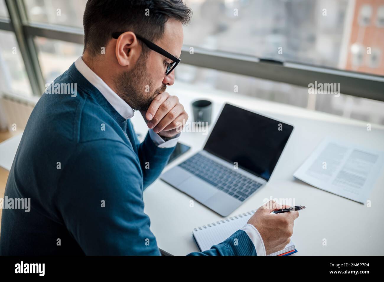 Thoughtful adult man, using a pen to write in the notebook, on his office desk. Stock Photo