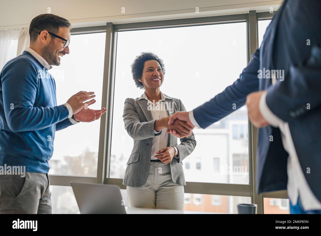 Smiling african american woman, handshaking with her colleague, while her male coworker claps. Stock Photo