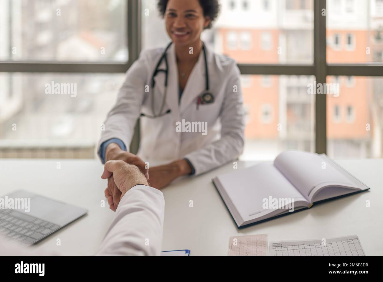 Excited adult female intern, wearing a stethoscope, starting work as a hospital intern, handshake. Stock Photo