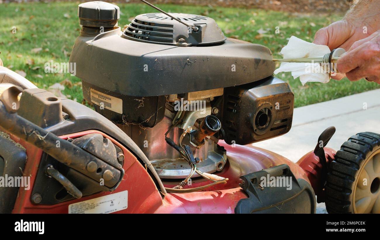 Male landscaper checking engine oil level on gas powered lawn mower. Checking dipstick for proper oil level. Stock Photo