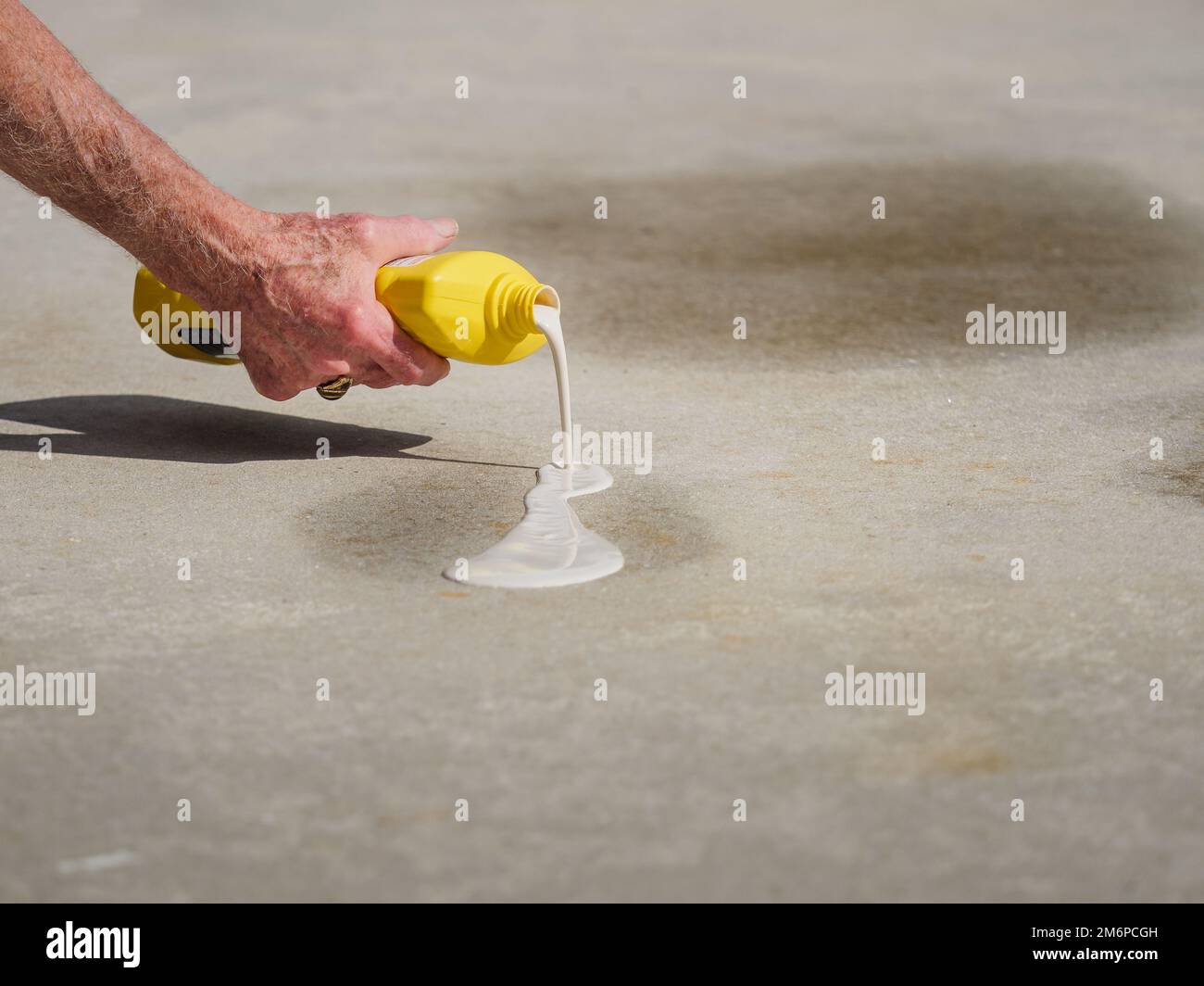 Man applying oil stain remover to concrete driveway. Removing automobile motor oil stains from parking spots with cleaning product. Stock Photo