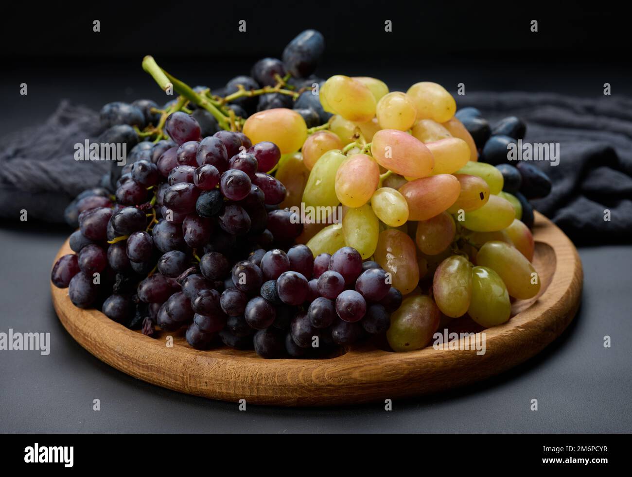 Black and green grapes in a wooden round plate on a black table Stock Photo
