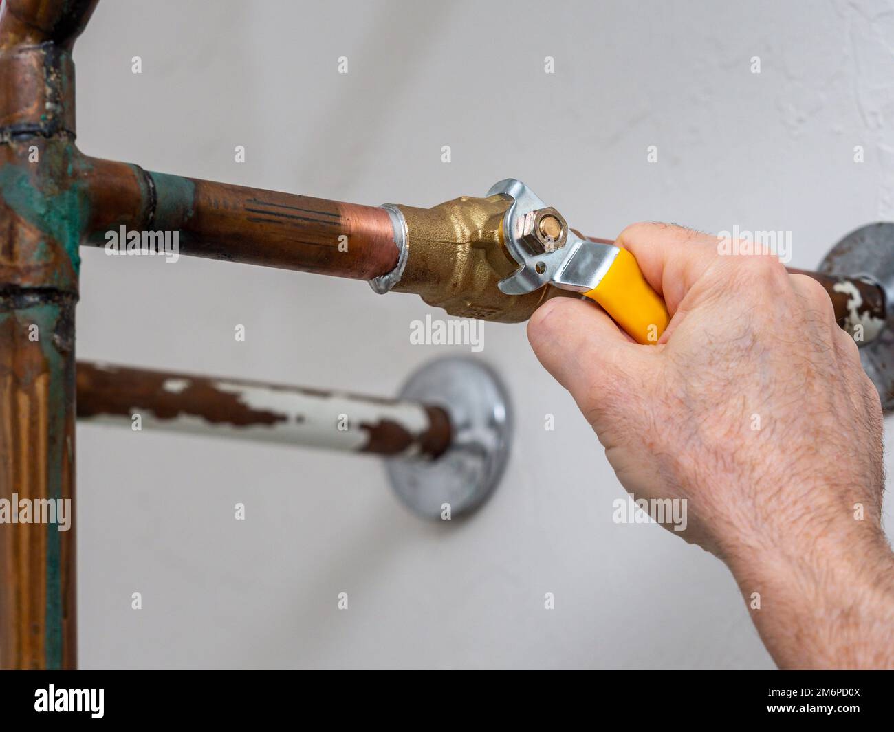 Plumber turning water shut off valve. Copper plumbing pipe with brass water supply valve and yellow stopcock handle. Stock Photo