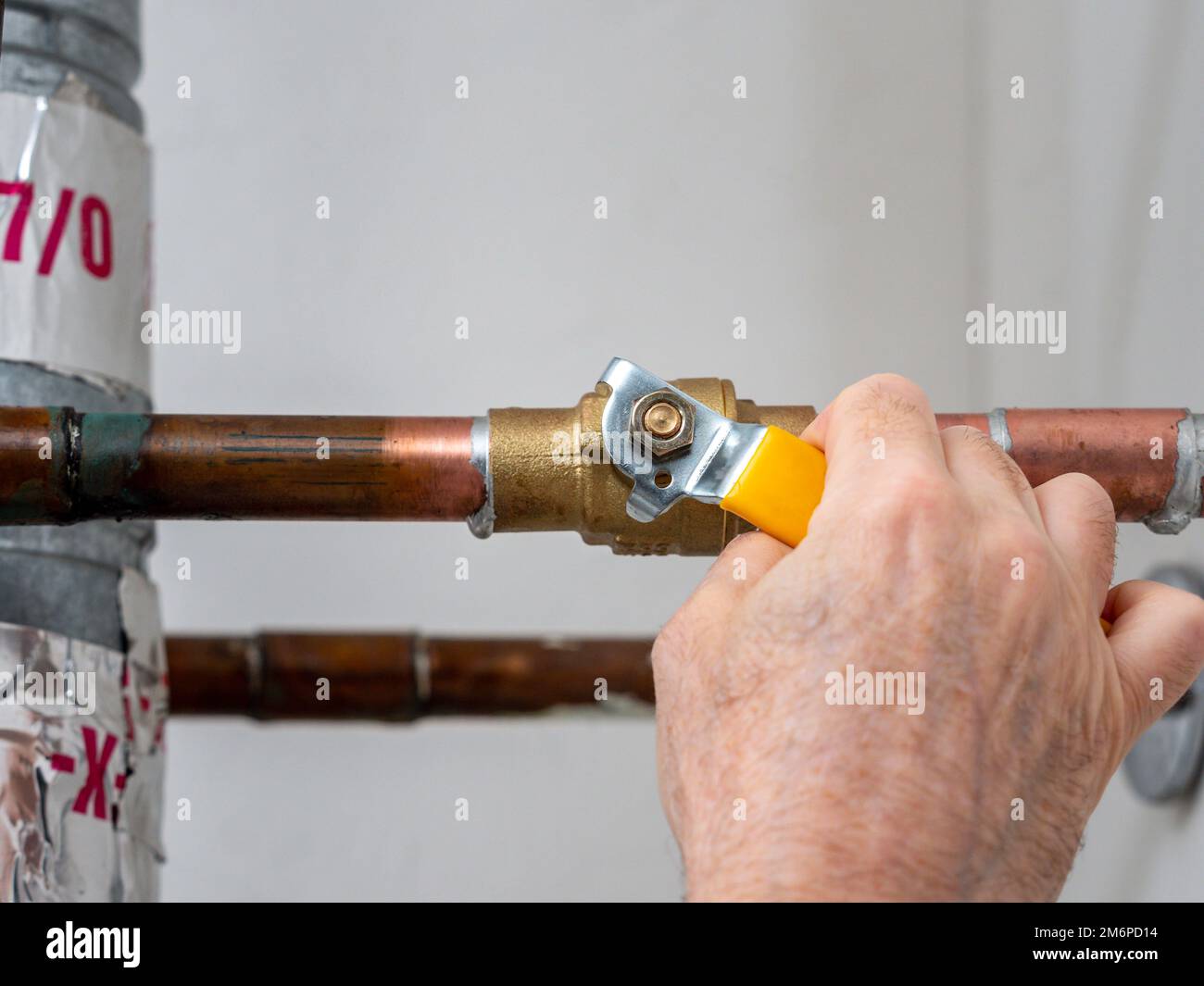 Plumber turning water shut off valve. Copper plumbing pipe with brass water supply valve and yellow stopcock handle. Stock Photo