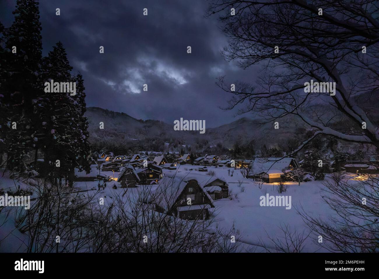 Lights from houses in traditional farming village in snowy valley at dusk Stock Photo