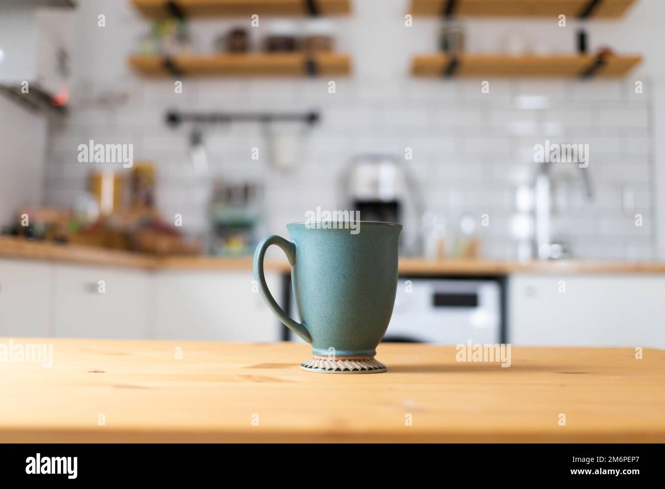Green coffee cup on kitchen table blurred kitchen in background Stock Photo