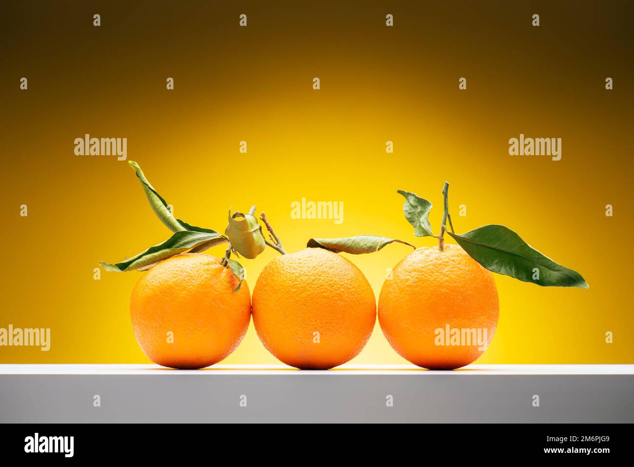 Fresh orange fruits with leaves on shelf on yellow background. Stock Photo