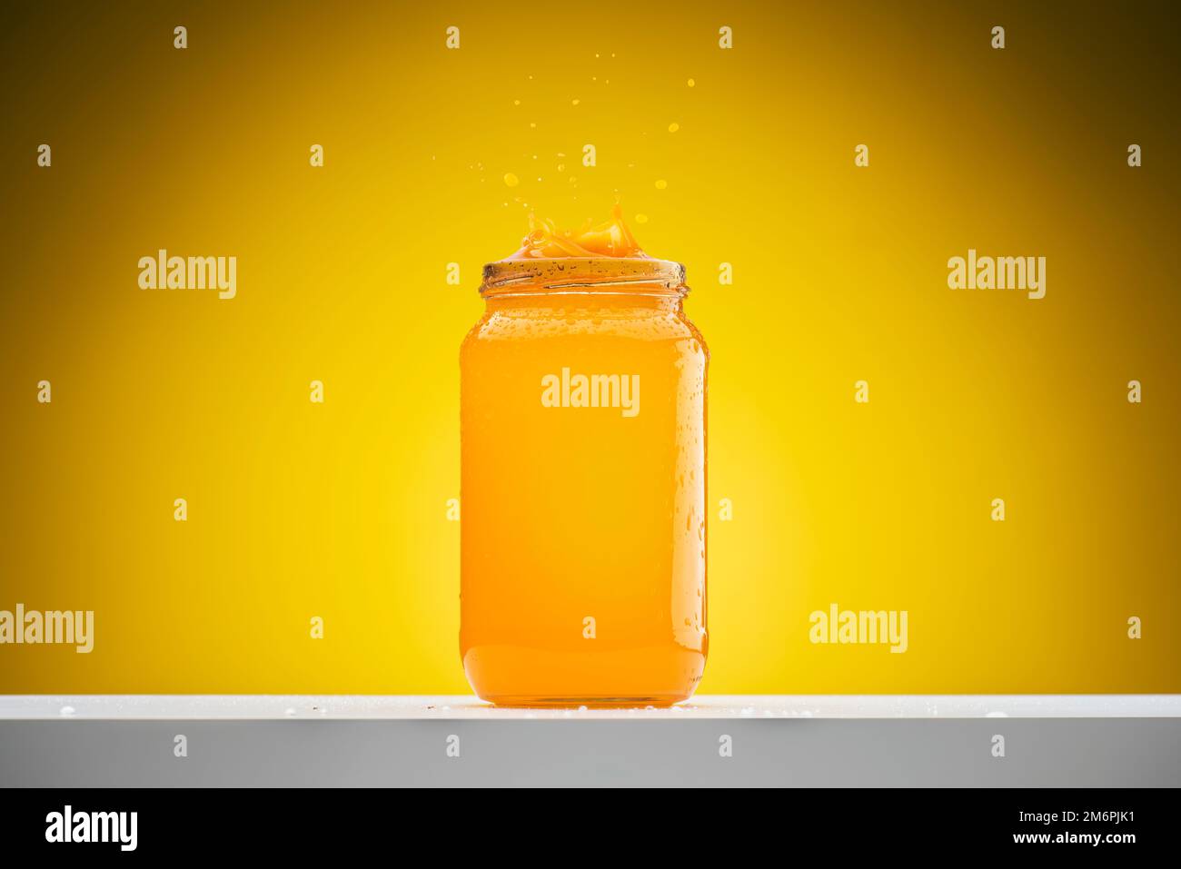 Fresh orange juice in glass jar with splash on shelf on yellow