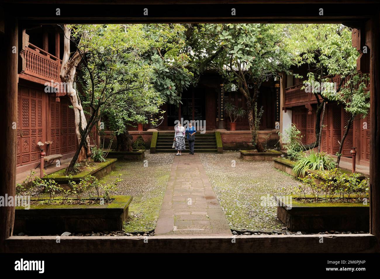 Traditional chinese courtyard house in Yunnan province. Ancient village house garden with trees. Chinese wooden screens on facade in courtyard. Stock Photo