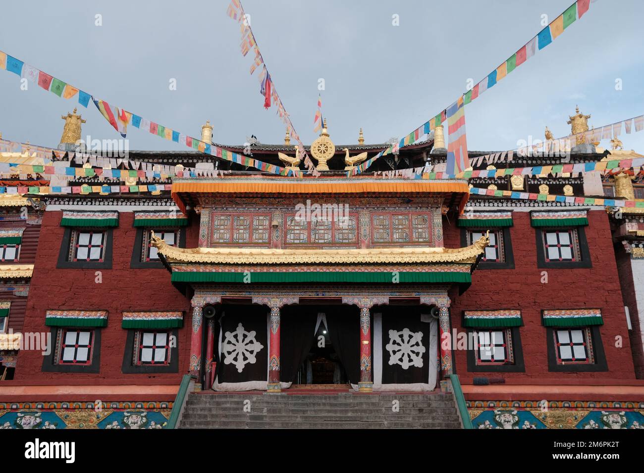 Tibetan architecture. Traditional tibetan buddhist temple with prayer flags in the sky. Buddhist temple red fasade with golden ornaments and symbols. Stock Photo