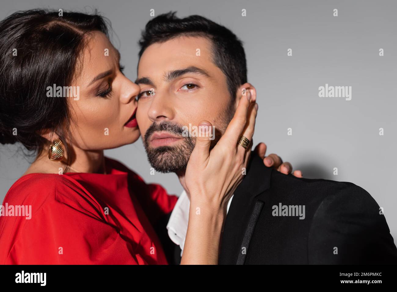 Elegant woman with makeup kissing boyfriend in formal wear on grey ...