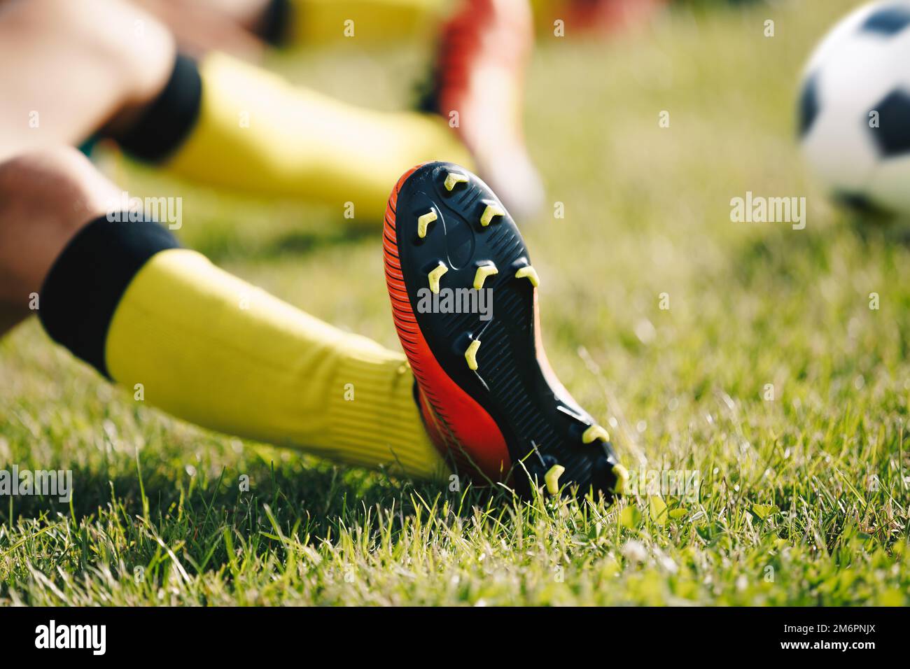 Teenage Boy Sitting and Stretching on Sports Grass Field. Soccer Ball in Background. Young