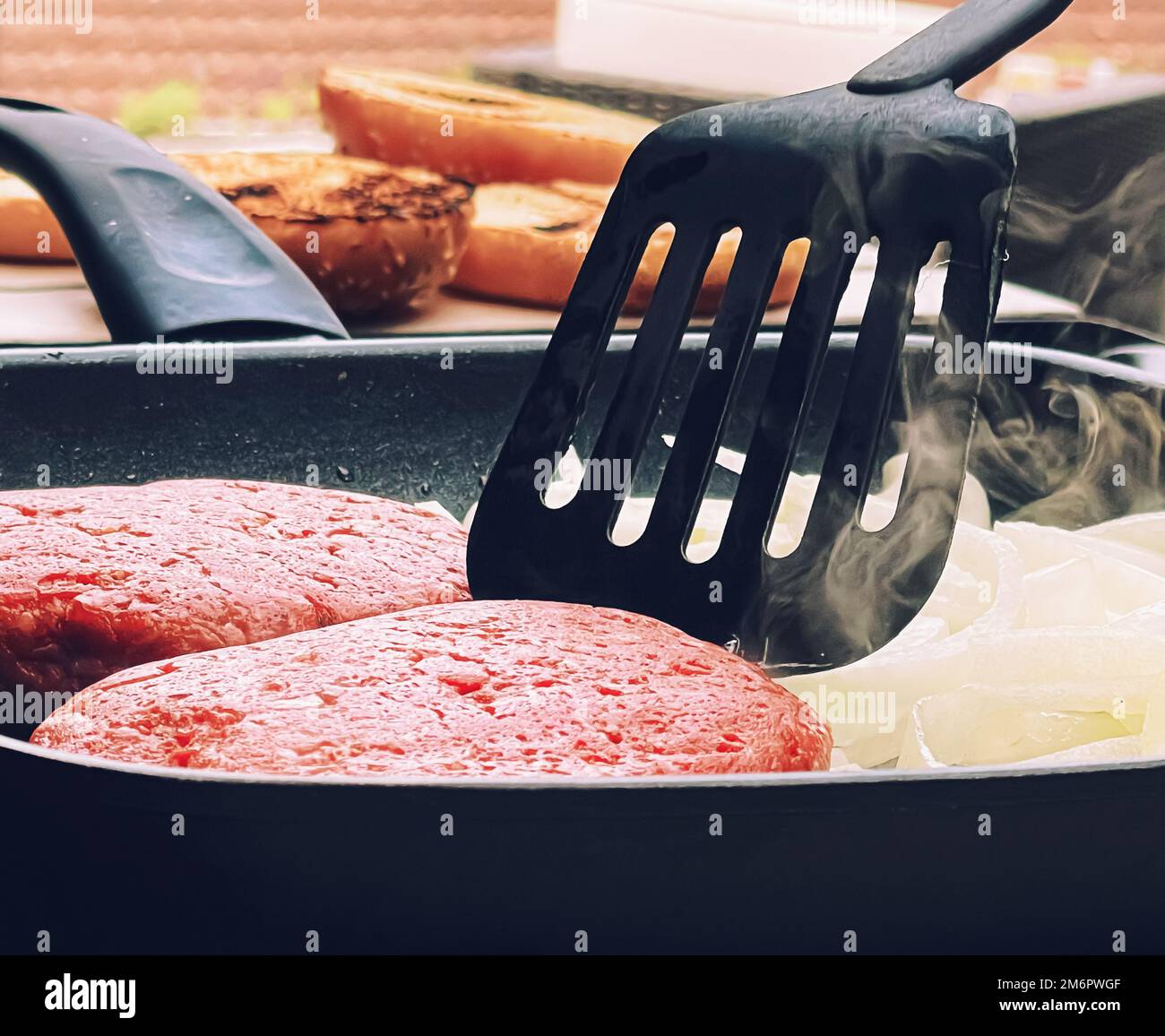 Cooking minced beef burger on cast iron grill skillet outdoors, red meat on frying pan, grilling food in the garden, English cou Stock Photo