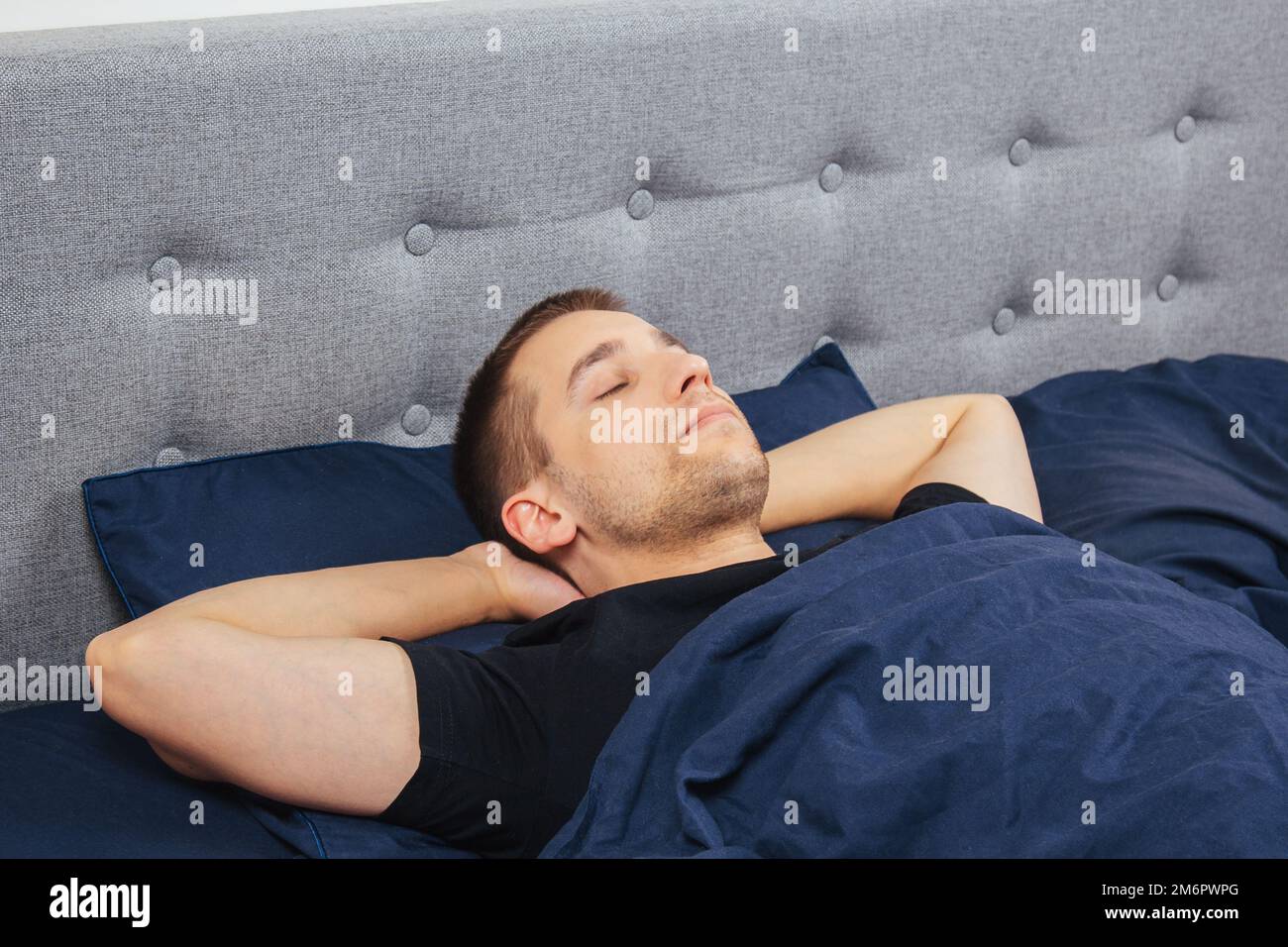 Top view of a handsome young man sleeping comfortably on the bed at night in his bedroom. Sleep in different positions. Bachelor bedroom. Deep sleep. Stock Photo