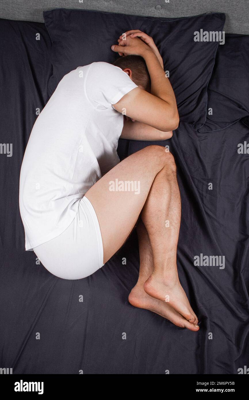 Handsome young man sleeping comfortably on the bed at night in his bedroom wearing pajamas. Bachelor bedroom. In the fetal position. Stock Photo