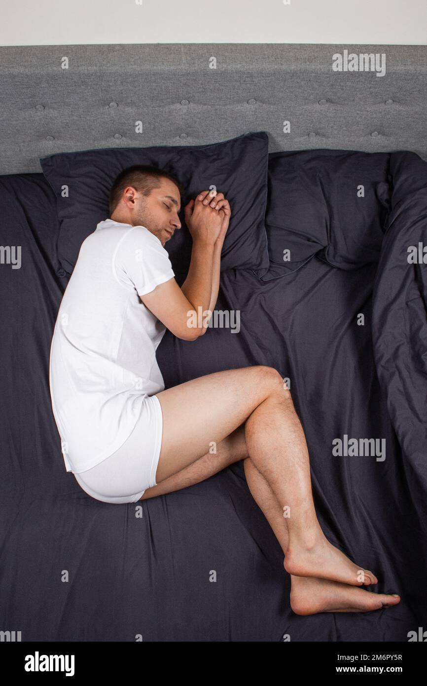 Handsome young man sleeping comfortably on the bed at night in his bedroom wearing pajamas. Bachelor bedroom. In the fetal position. Stock Photo