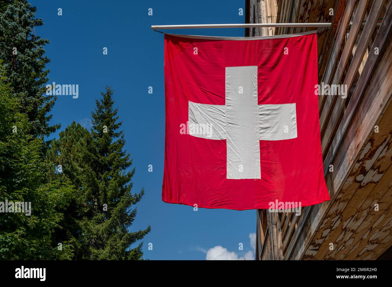 Swiss flag. Switzerland flag hanging on roof against blue sky. One red square flag with a white cross in the centre. Stock Photo