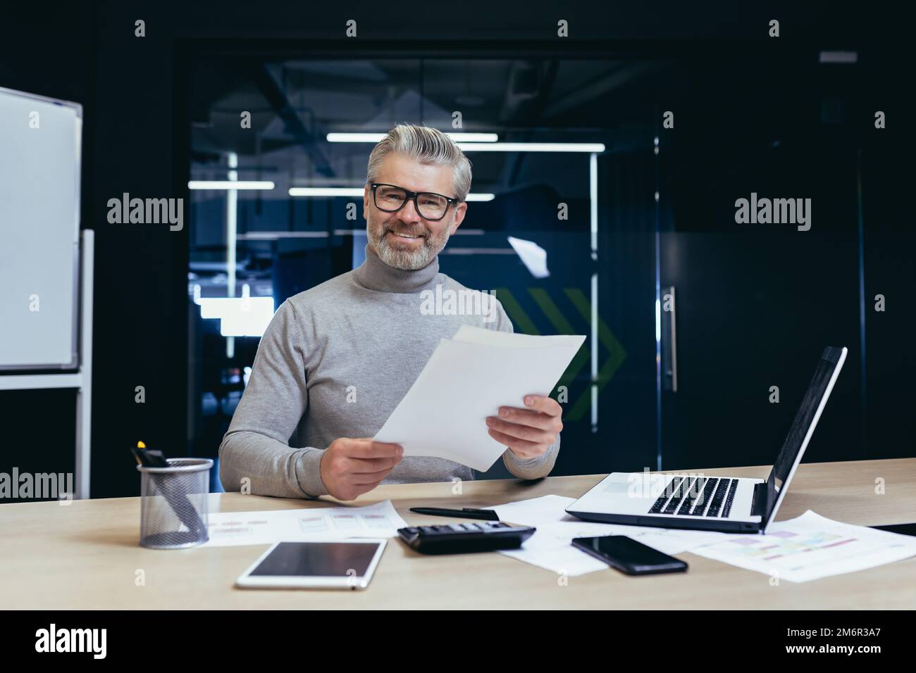 Successful businessman with documents smiling and looking at camera, portrait of mature gray-haired investor financier inside modern office, man behind paper work with reports accounts and contracts Stock Photo