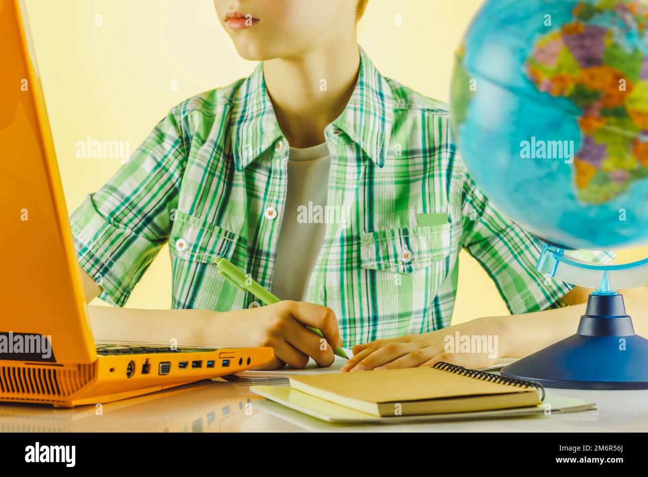 Online learning lifestyle with teenager boy using laptop, studying online at home. Schoolboy writing in notebook, looking at pc screen, watching webin Stock Photo